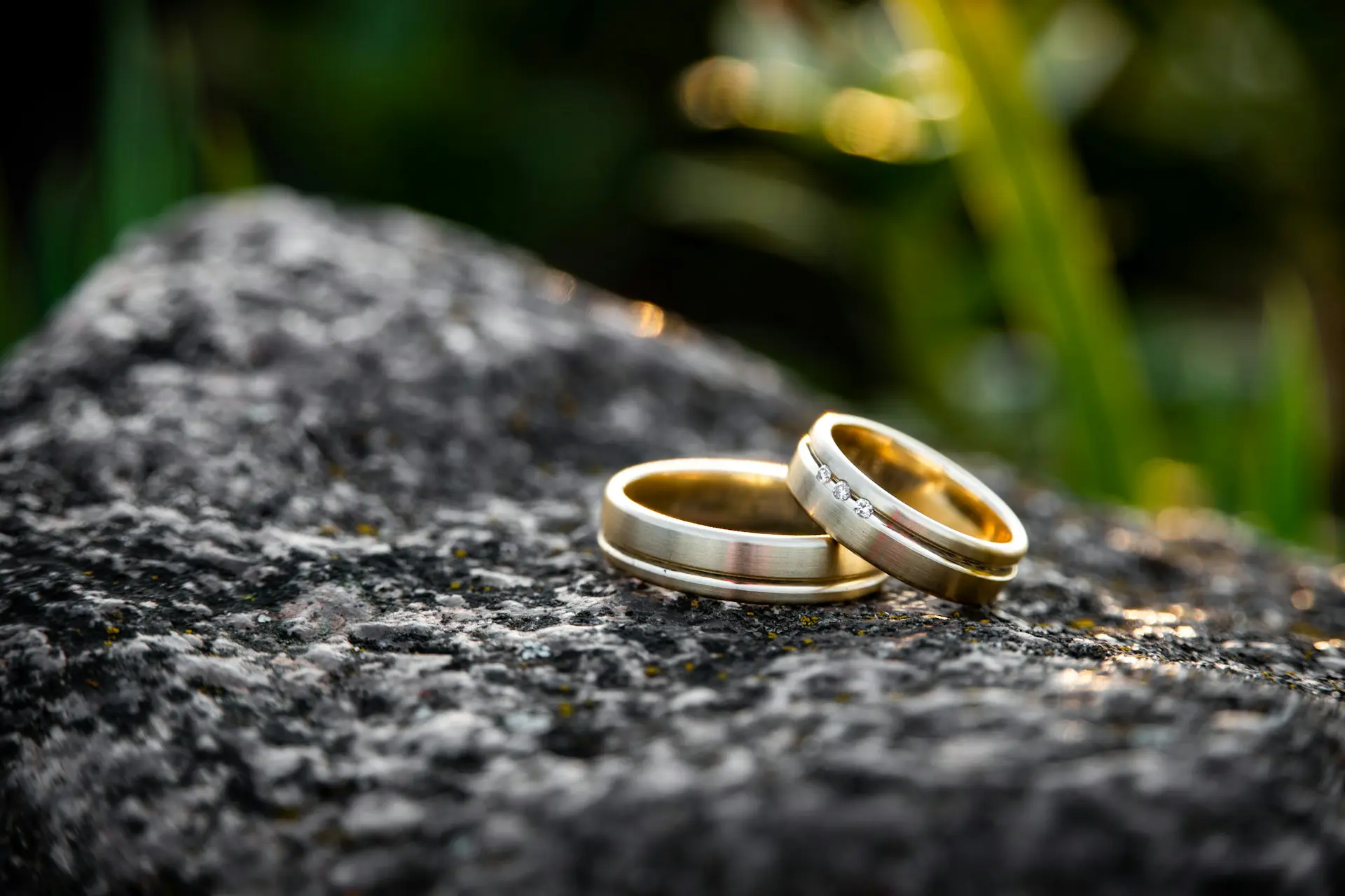Two gold-band wedding rings on top of a black rock
