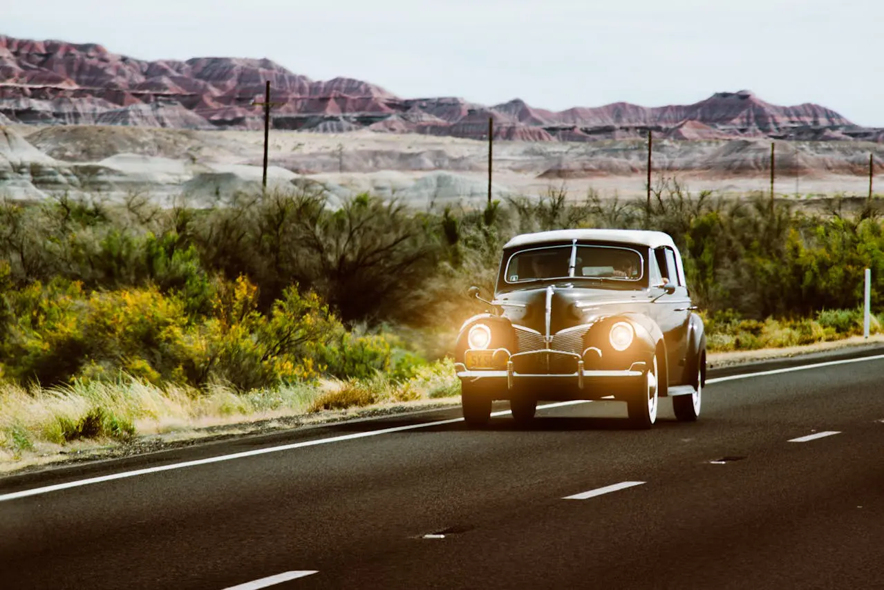 Black vintage car driving with headlights on with Arizona mountains in the background