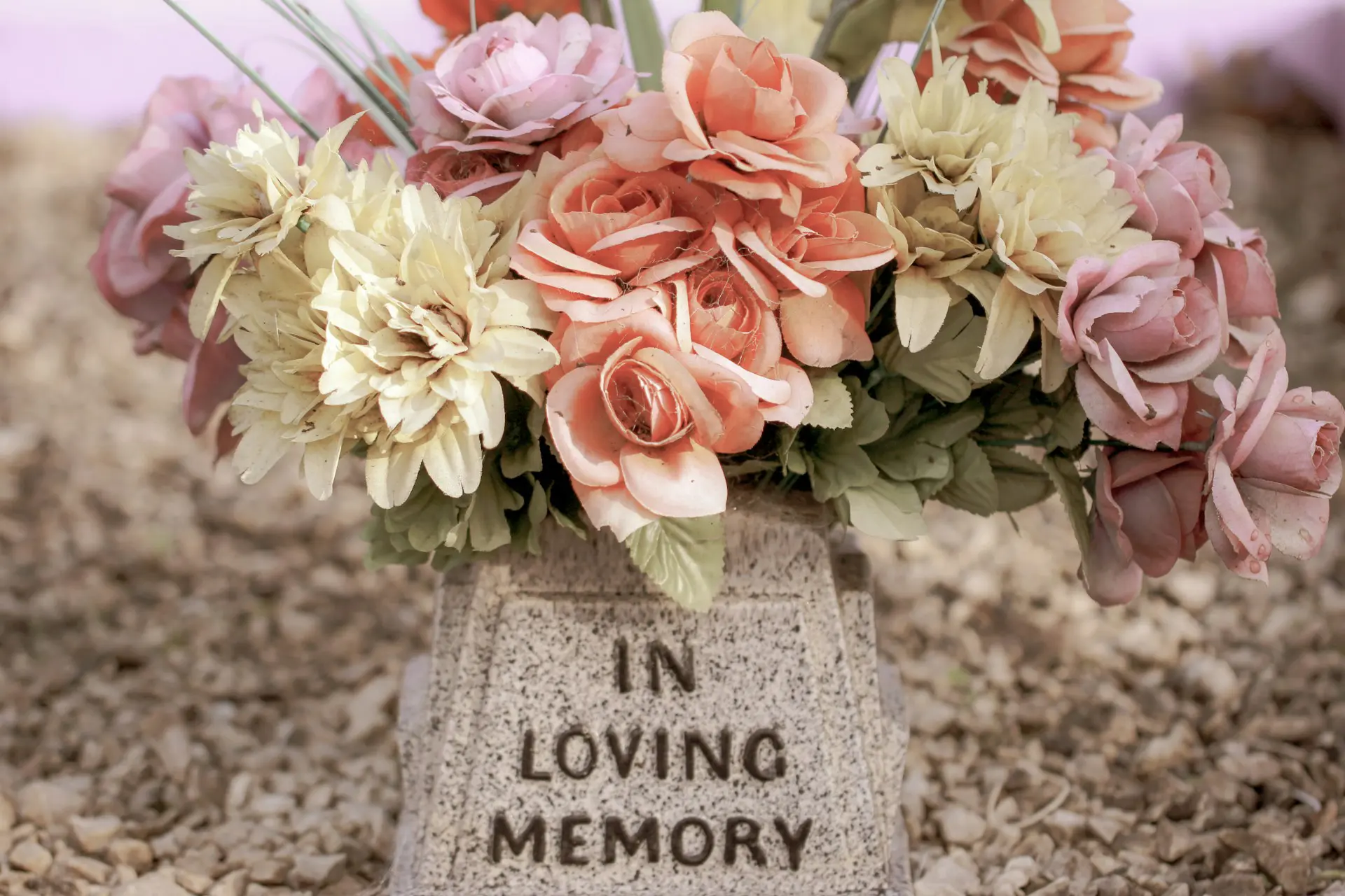 Pastel flowers resting on a memorial stone that reads "In Loving Memory"