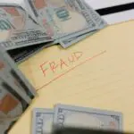 The word 'Fraud' written in red on a yellow paper surrounded by money.