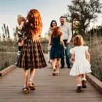 A mother and father standing on a bridge while their four young children run to them.