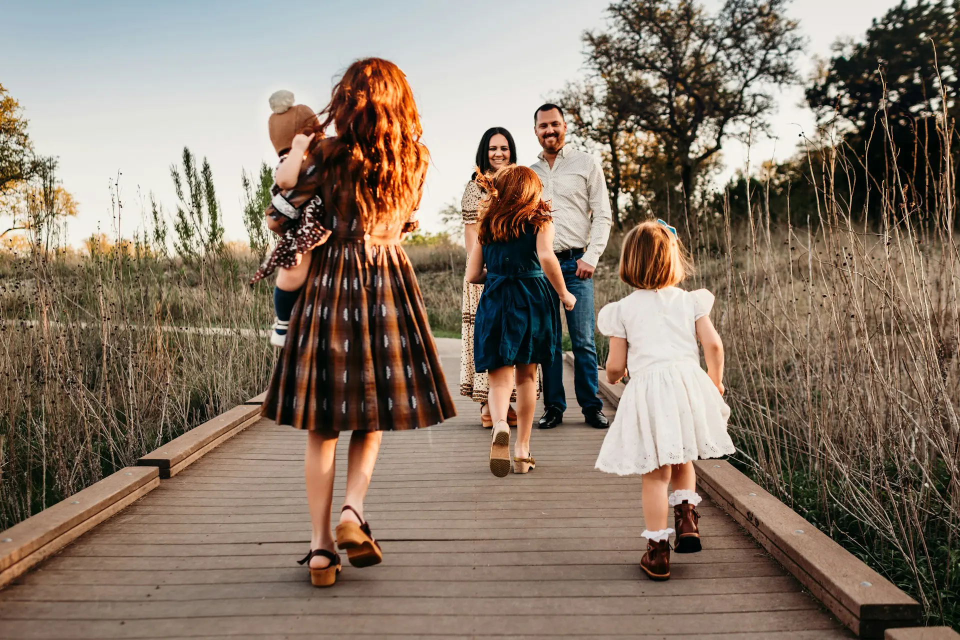 A mother and father standing on a bridge while their four young children run to them.