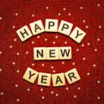 Red background with gold stars and scrabble tiles that read "Happy New Year"
