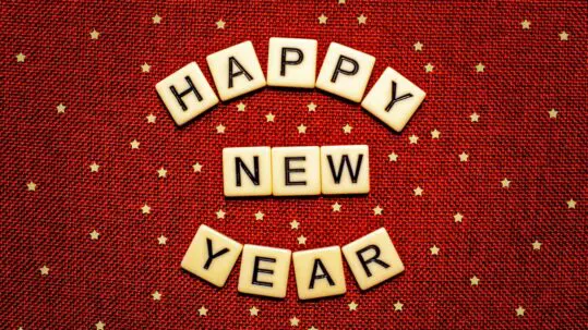Red background with gold stars and scrabble tiles that read "Happy New Year"
