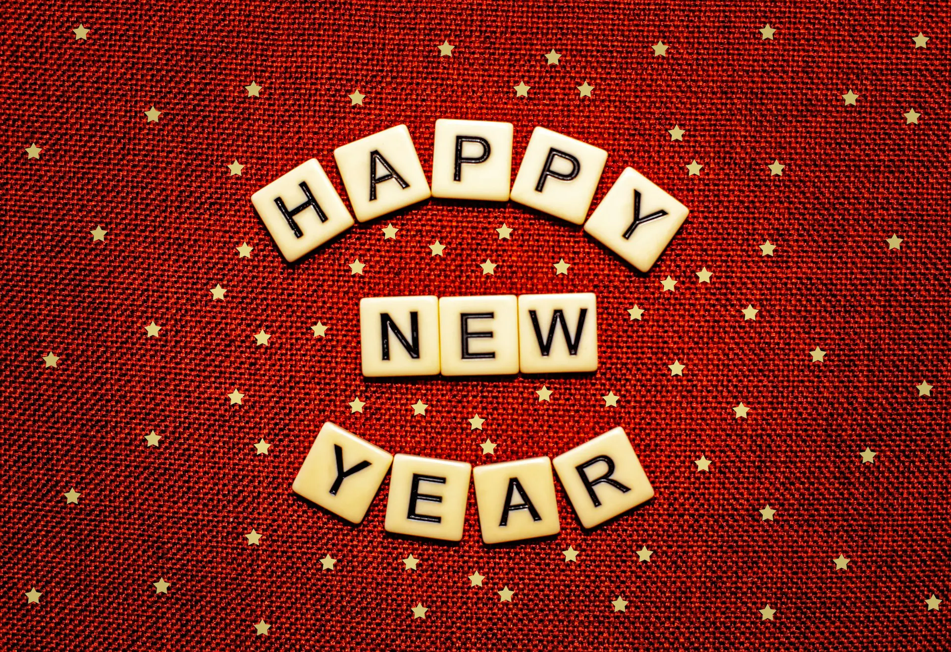 Red background with gold stars and scrabble tiles that read "Happy New Year"