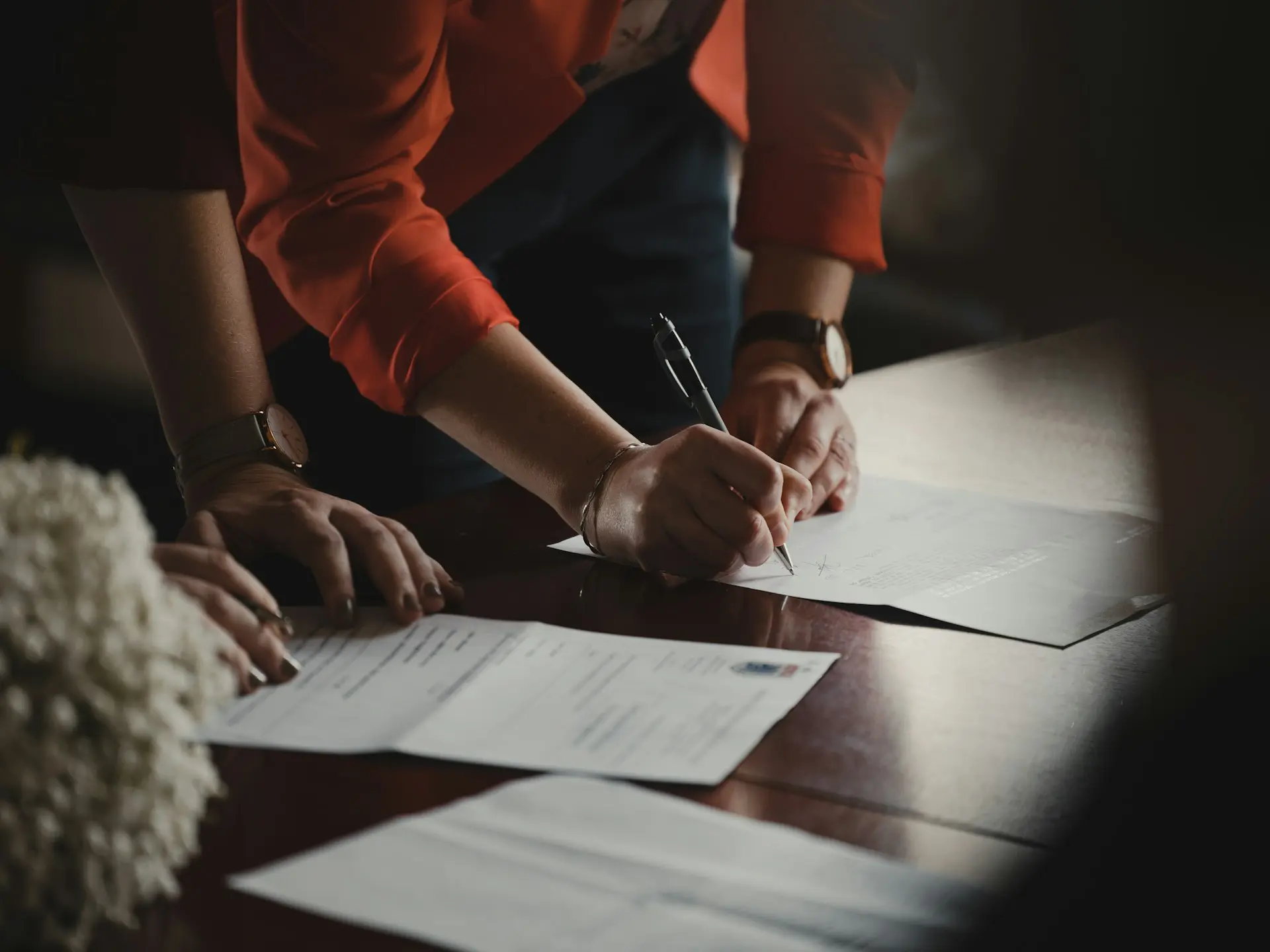 Close-up of two people signing paperwork at a desk.