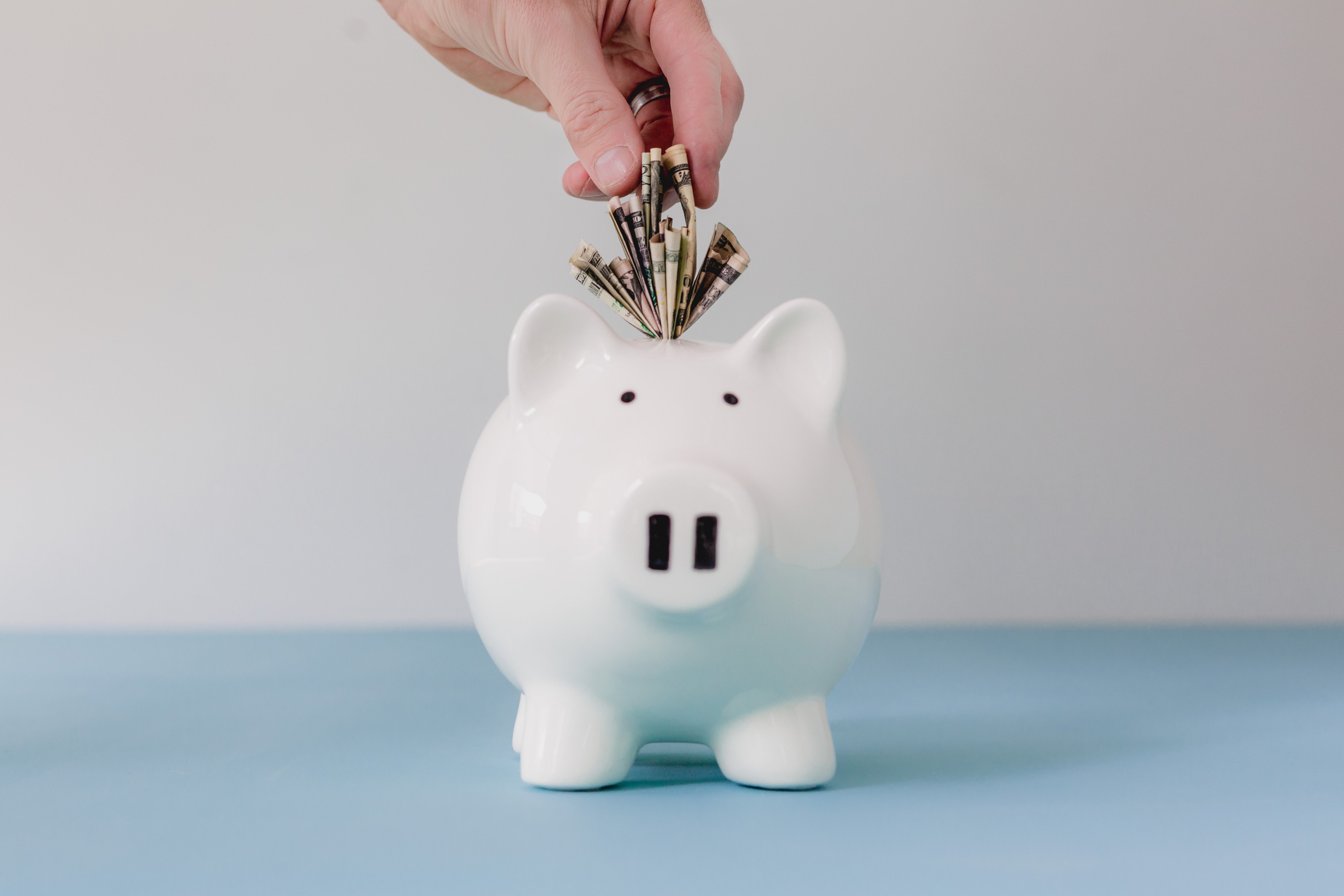 keys for raising financially responsible children - hand stuffing dollar bills into a piggy bank
