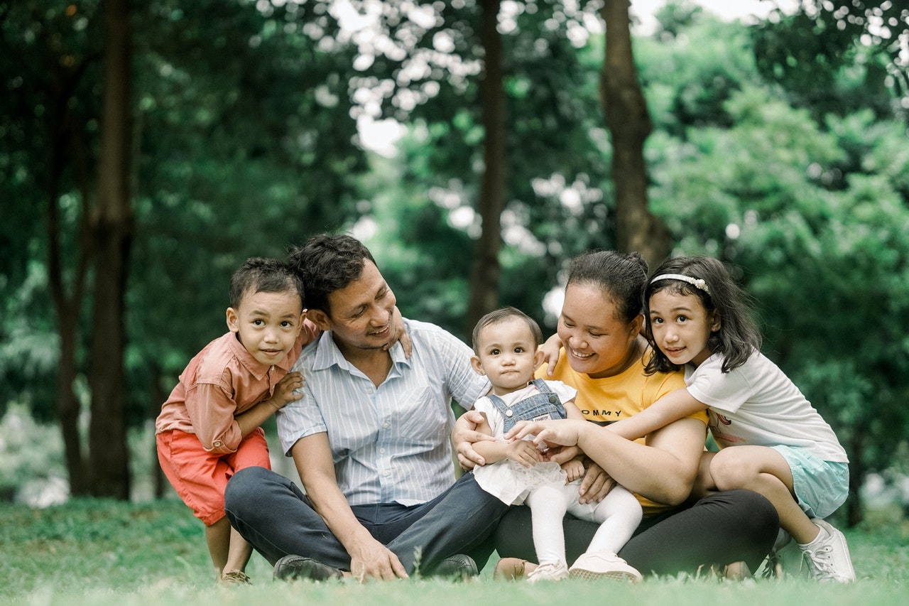 estate planning with life insurance -- family of mother, father, and three children sitting on a grass and hugging each other