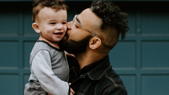 father kissing toddler son on cheek