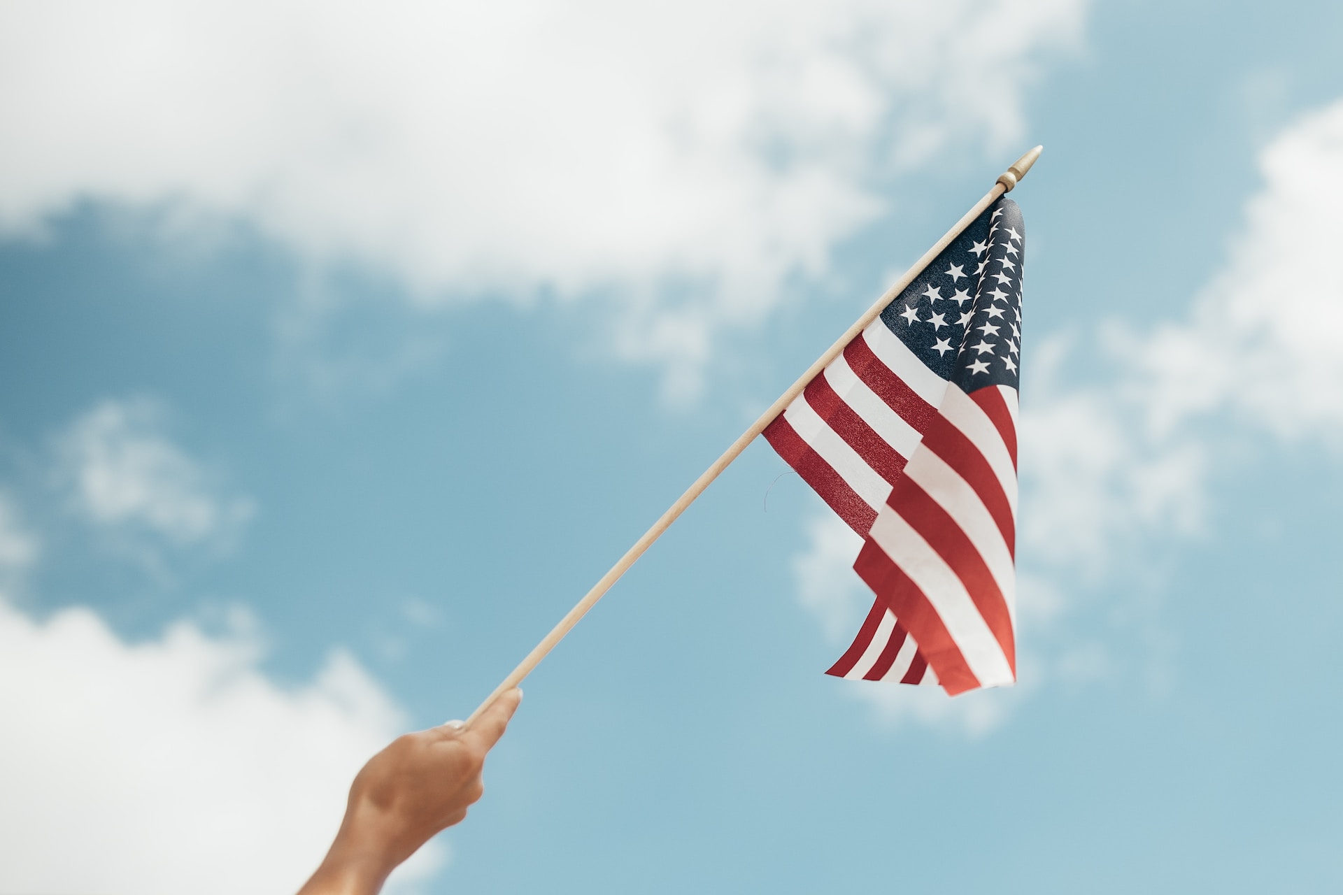 person holding up american flag with cloudy sky background