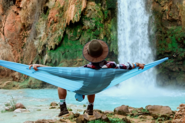 person lounging in hammock next to waterfall