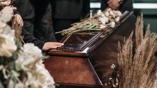 a hand and flowers placed on casket at funeral