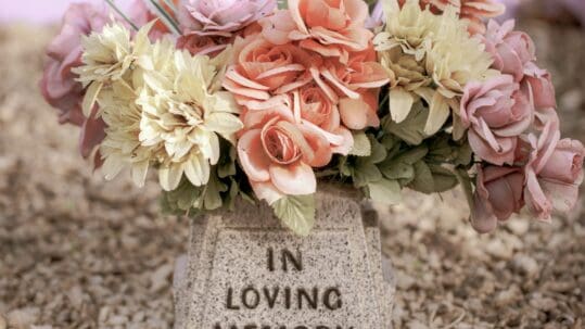 Pastel flowers resting on a memorial stone that reads "In Loving Memory"